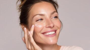 A woman smiling while applying a cream to her face photo