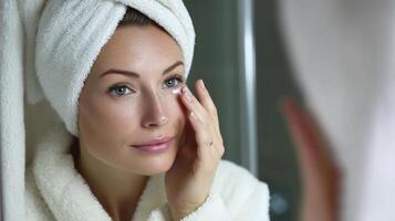 A woman in a bathrobe looking at her face in the mirror photo