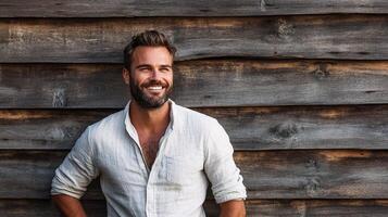 A man with a beard and white shirt standing in front of a wooden wall photo
