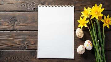 Blank notebook with Easter eggs and daffodils on dark wooden table background. Space for text photo