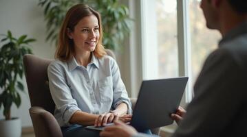 A smiling woman in a blue shirt listens attentively during a professional meeting in a modern office with natural light and greenery. Business concept photo