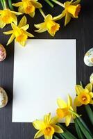 Yellow daffodils and painted Easter eggs decorating white paper on dark wooden background, flat lay with spring and festive holiday concept Space for text photo