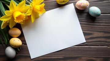 Yellow daffodils and colorful Easter eggs surround a blank white card on a rustic wood table, symbolizing spring or Easter celebration photo