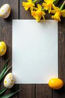 Blank white sheet surrounded by painted Easter eggs and yellow daffodils on a dark wooden table, perfect for spring or Easter-themed designs Space for text photo