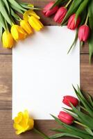 Yellow and red tulips arranged around a blank white paper sheet on a wooden table background, symbolizing spring, floral decor, invitations photo
