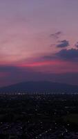 Vertical footage, aerial view of a city at twilight with a colorful sunset sky and distant mountains, highlighting the serene beauty of urban landscapes. video