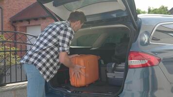 Man loading orange suitcase into car trunk before journey video