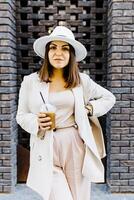 Portrait of successful business woman holding cup of cold drink in hand on her way to work on city street. photo