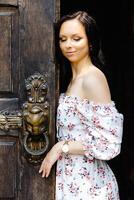 A young beautiful woman is standing near an open old door, smiling and looking at the camera photo