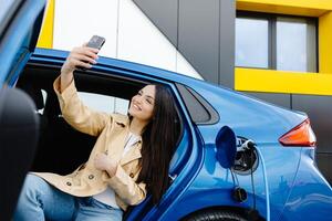 Business lady sitting inside charging electric car and using modern smartphone. photo