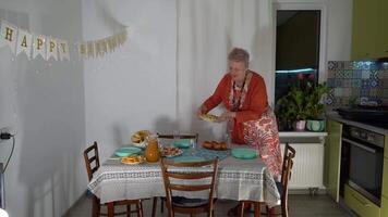 An elderly woman sets the table. A grandmother is expecting guests for a birthday party and preparing food. Putting plates on the table. Table setting. video