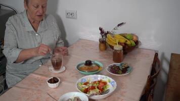 Stir the tea bag with a teaspoon. Elderly woman drinks tea at the table. Food on plates. Lunch at home in the kitchen of grandma video