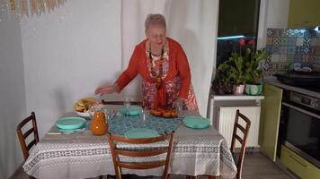 An elderly woman sets the table. A grandmother is expecting guests for a birthday party and preparing fruit food. Putting plates on the table. Table setting. video
