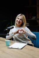 Smiling woman making heart shape with hands during podcast recording photo