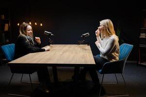 Two female podcasters having a conversation, recording audio in a studio photo