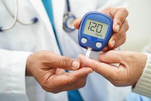 Asian doctor using digital glucose meter for check sample blood sugar level to treatment diab photo
