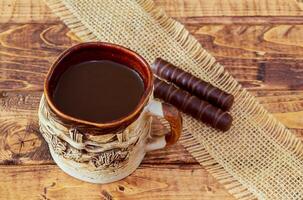 coffee cup and beans, cinnamon sticks, nuts and chocolate on wooden table on brown background photo