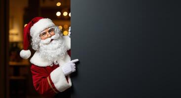 Santa Claus peeking from the left side of a large vertical dark gray sign, pointing towards the board with his right hand. Christmas concept. photo