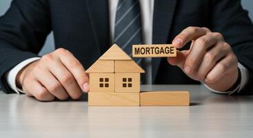 Businessman holds a wooden block with the word mortgage. A wooden house assembled from blocks symbolizes real estate and home ownership. Investment and finance concept. photo