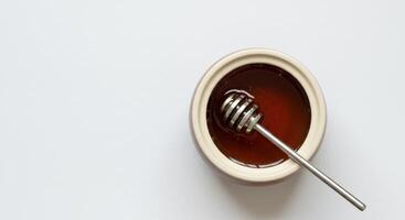Overhead shot of a bowl of honey with a honey dipper on white background. Copy space to the left. Sweet food concept. photo