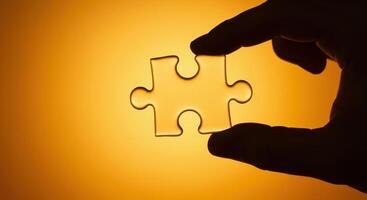Businessman holds a puzzle piece in his hand against an orange background, symbolizing solutions, teamwork, and strategic thinking in business. photo