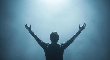 Rear view of man with arms outstretched upwards into a hazy illuminated sky. Soft ethereal texture with swirling light effects in the background. photo