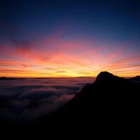 A sunset over the clouds with a mountain in the foreground photo