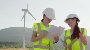 Two engineers in safety gear are onsite at a wind farm, reviewing plans and collaborating to advance sustainable technology and innovative green energy solutions for a cleaner future video