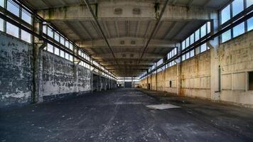 Empty industrial hall stretching into the distance with peeling walls and large overhead windows photo