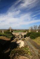 Ornate stone bridge at castle Roseburg framed by statues and green hedges with open countryside beyond photo