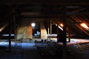Dusty attic space with exposed wooden beams, brick archway, and scattered remnants of the past photo