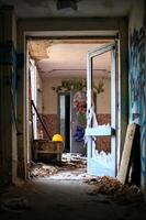 Broken doorway leading through an abandoned building with yellow helmet and scattered debris photo
