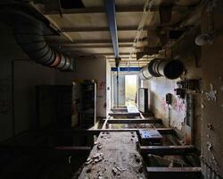 Abandoned industrial space with rusted pipes, broken flooring, graffiti, and exposed ventilation ducts photo