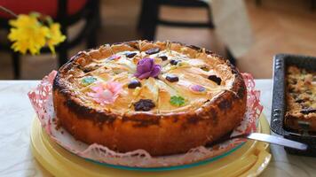 Decorated apple cake with chocolate and sugar flowers on a table with another baked pastry photo