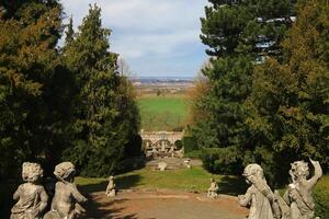 Statues framing Roseburg garden view in Germany, with distant town beyond green fields and formal tree borders photo