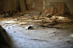 Damaged bulging floor covered in torn paper, dust, and debris inside an abandoned and neglected room photo