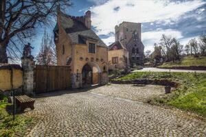 Castle Roseburg courtyard gate with cobbled path and sunlit tower under a partly cloudy sky photo