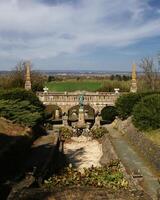 Stone terrace fountain of Castle Roseburg overlooking green fields under a wide blue sky with distant hills photo