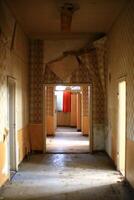 Peeling wallpaper hallway leading to a distant room with an orange curtain and scattered debris photo