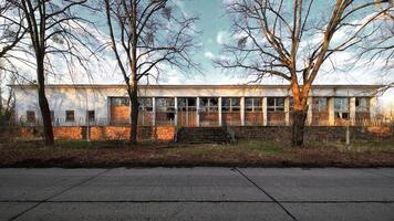 Deteriorating white structure with shattered glass surrounded by bare trees in afternoon light photo