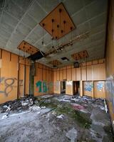 Decay and debris in an abandoned room with broken ceiling panels, graffiti, and scattered papers photo