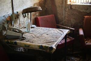 Dusty table with a rotary phone, empty bottle, and rusted lamp in an abandoned interior photo