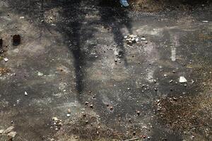 Shadowed concrete ground with scattered rubble, dry brush, and faint surface markings photo