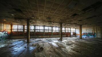 Dilapidated industrial hall with broken windows, graffiti-covered walls, and scattered debris photo