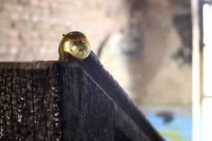 Burnt wood railing topped with brass sphere inside decayed interior space photo
