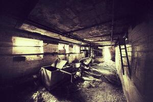 Dark abandoned basement with rusted pipes, broken equipment, and scattered debris on the floor photo