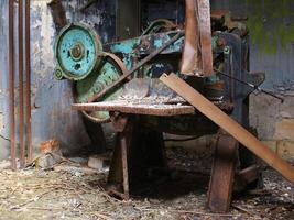 Rusted industrial machine in abandoned workshop surrounded by debris and peeling paint photo