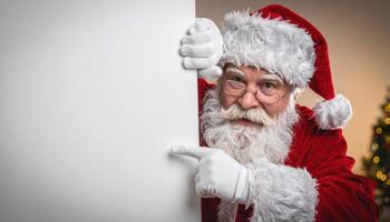 Santa Claus peeking from behind a large white sign, wearing red suit and hat, pointing to the blank space. Christmas tree in background. photo