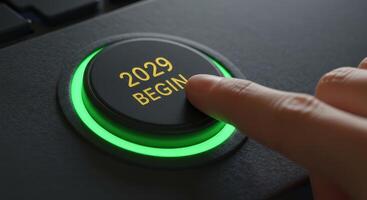 Finger presses a glowing green button labeled 2029 BEGIN on a dark keyboard. Symbolizes starting a new year, project, or initiative in 2029. photo