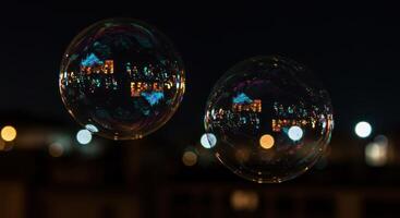 Two soap bubbles float with city lights reflecting on their surface, creating an urban abstract and adding a touch of whimsy to the night scene. photo